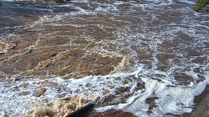Camera view of the same crossing under fast-flowing flood water